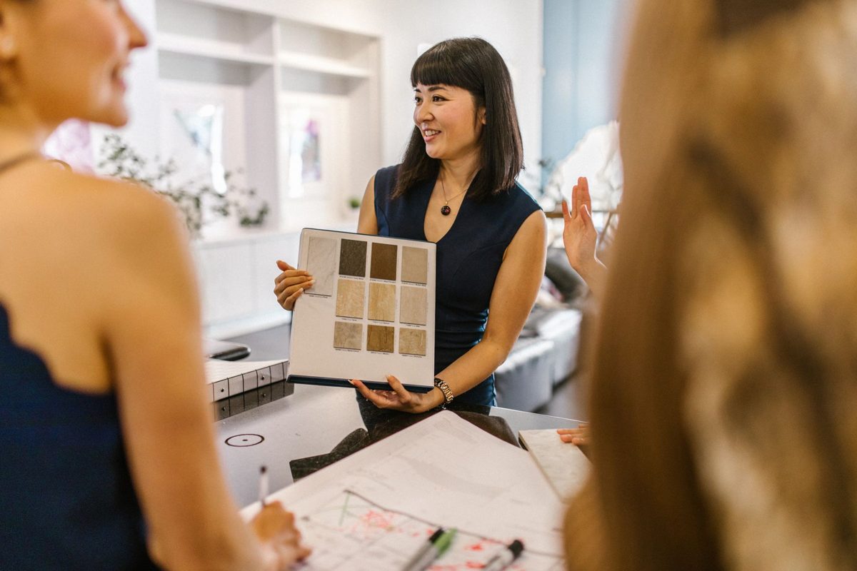 A designer holds up a board of finish samples to a couple across a table
